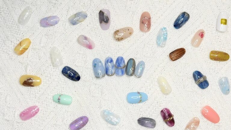 Assortment of colorful artificial nails with gradient, marble, and foil designs laid on a white towel.