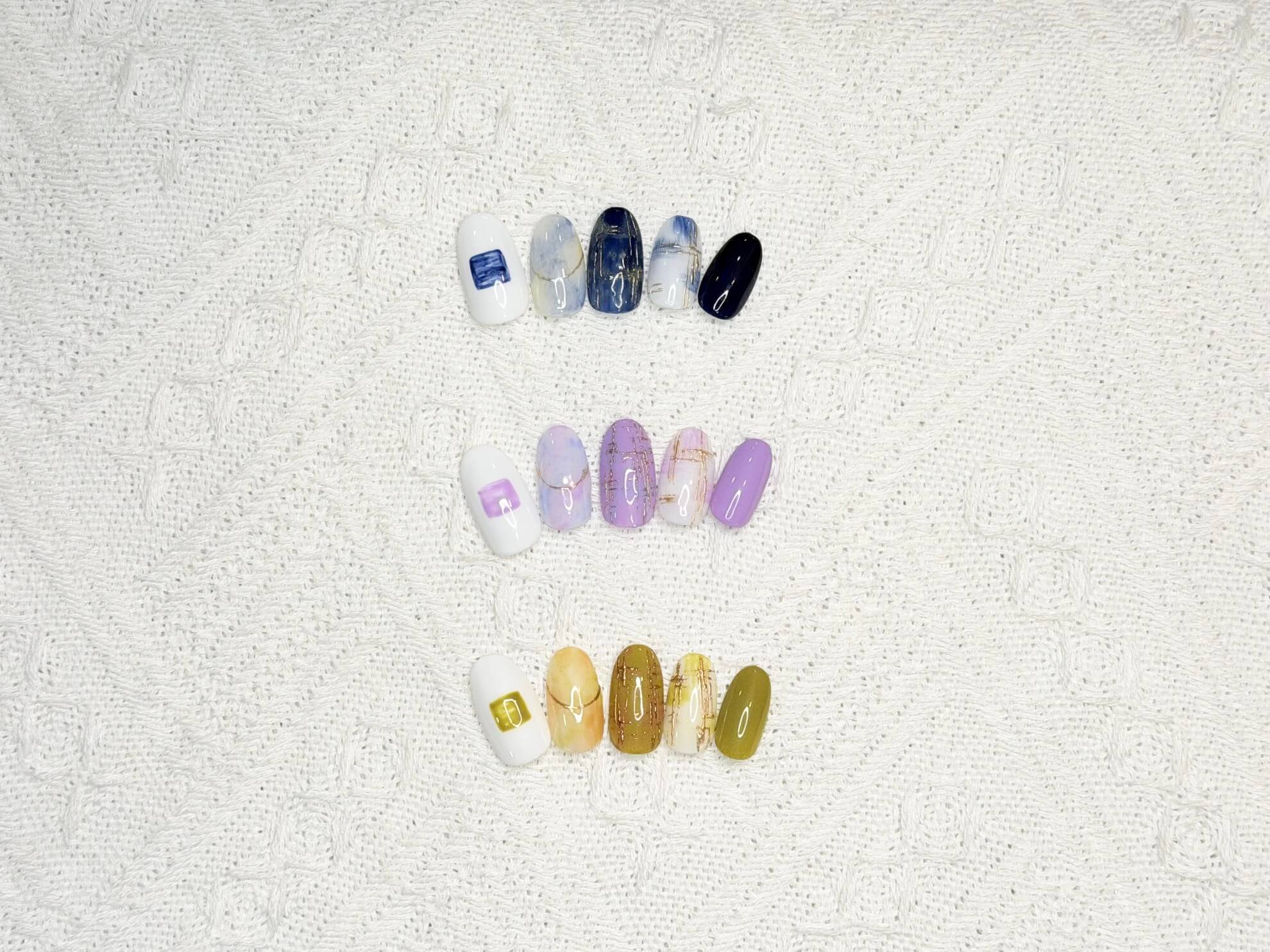 Row of artificial nail tips with blue-to-white ombre designs on a textured white towel surface.