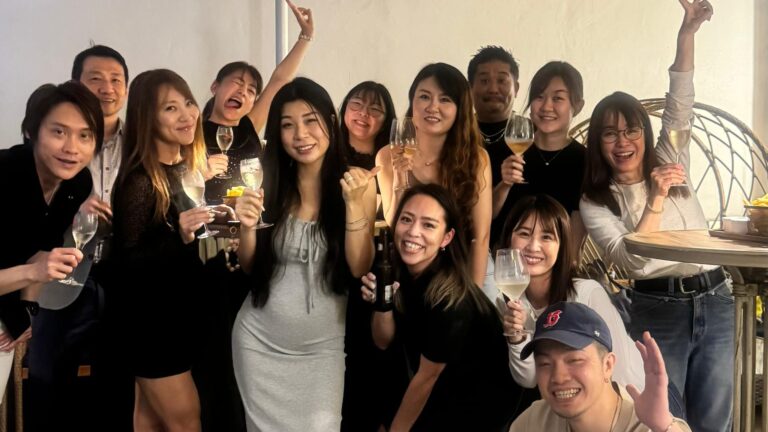 A joyful group of friends posing with wine glasses for a celebration indoors outdoors setup, smiling at the camera.